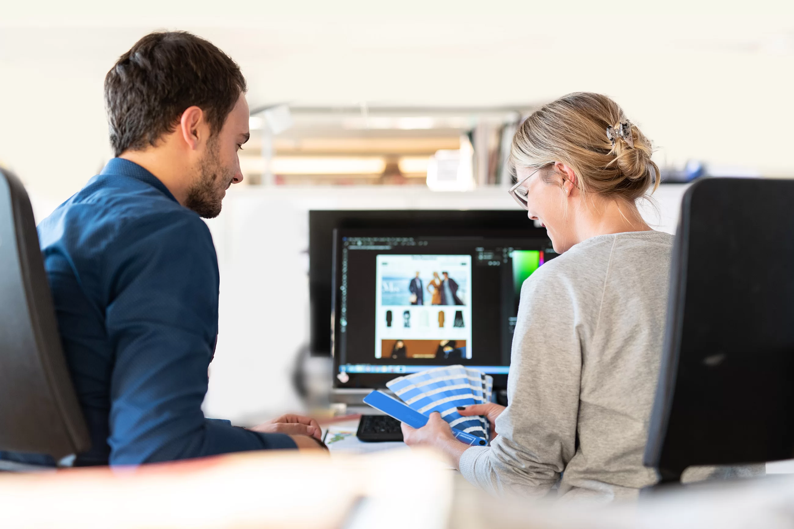 Ein Mann und eine Frau im Büro von hinten schauen auf einen Farbfächer