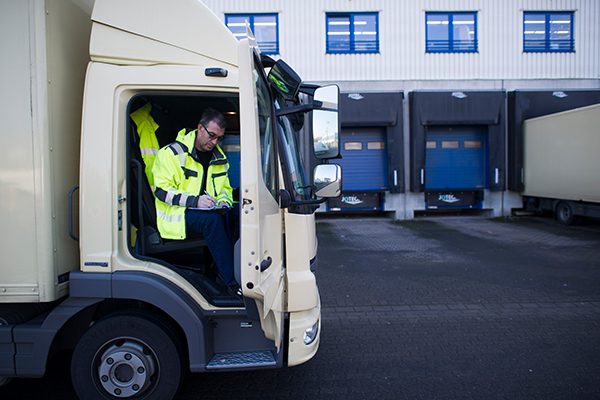 Am Firmengelände sitzt ein Logistikmeister bei offener Tür im LKW und bearbeitet ein Papier