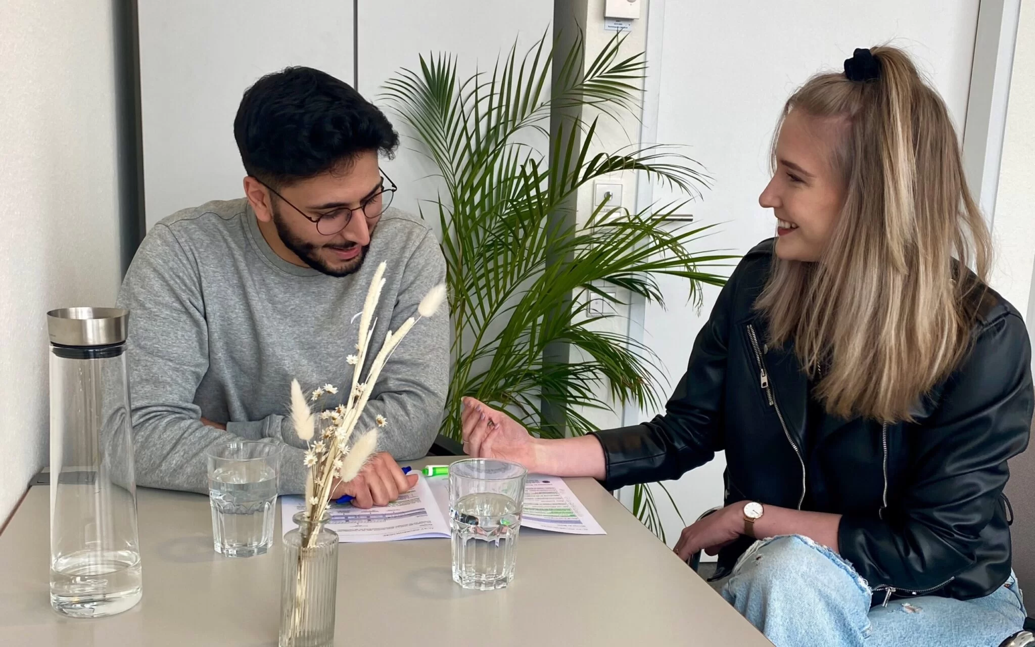 Katharina sitzt zusammen mit einem Kollegen am Tisch und schaut sich Unterlagen an. 