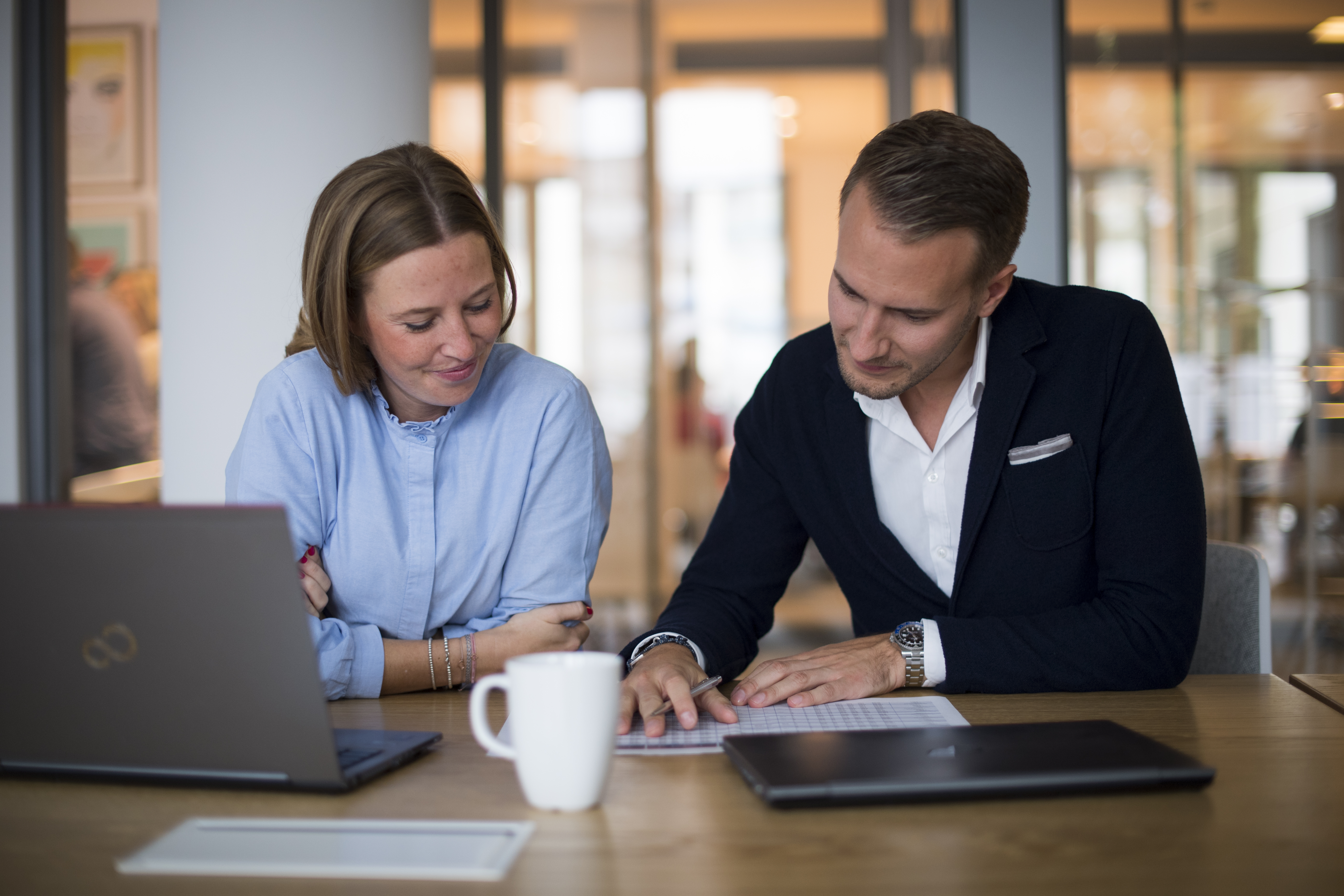 Ein Mann und eine Frau sitzen in einem modernen Büro mit einem Laptop und einem Becher und schauen auf  ein Dokument