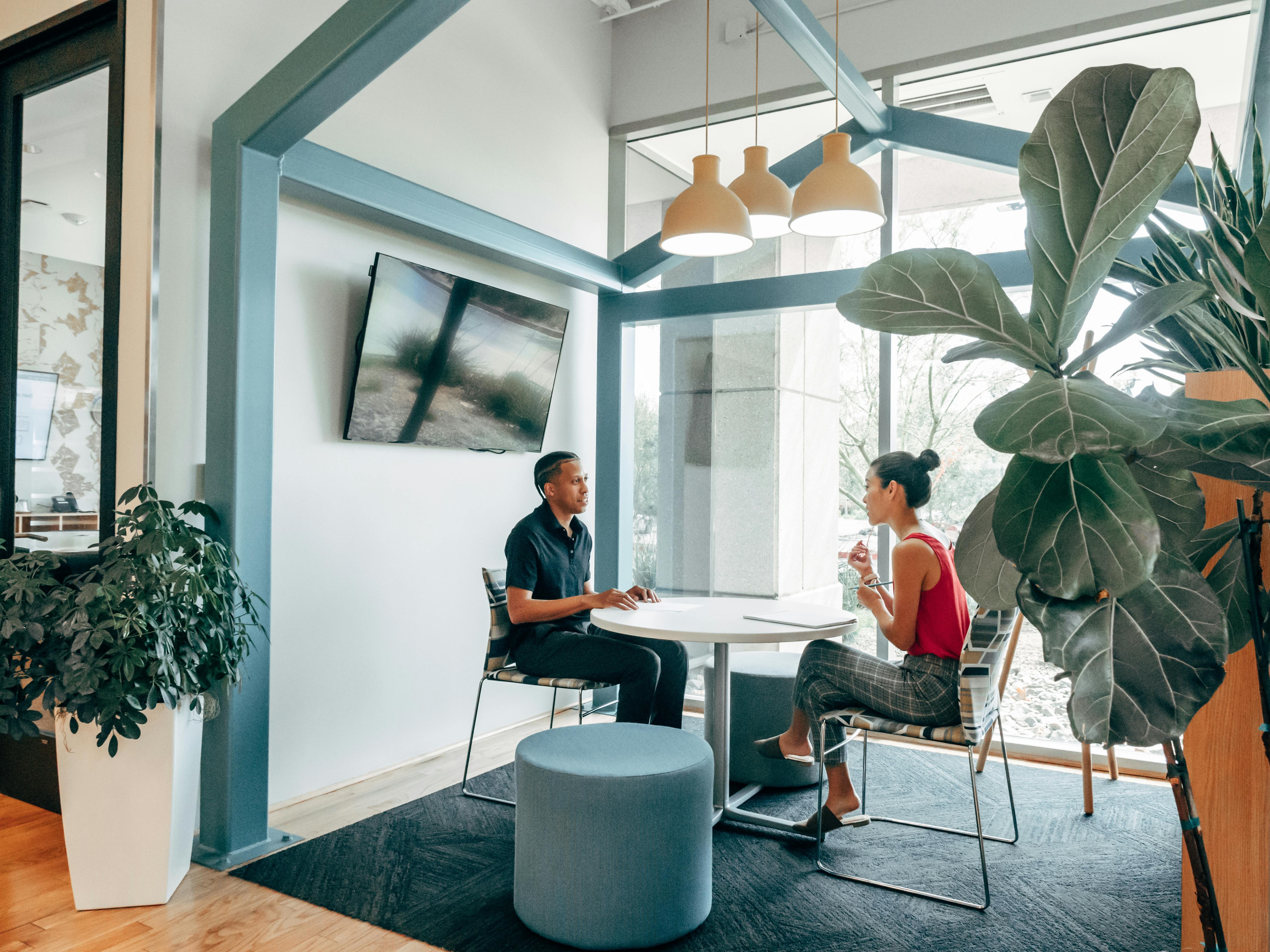 Ein Mann und eine Frau sitzen sich an einem Tisch in einem gemütlichen Workspace gegenüber und unterhalten sich.